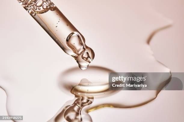 Glass dropper releasing a skincare serum droplet onto a reflective surface