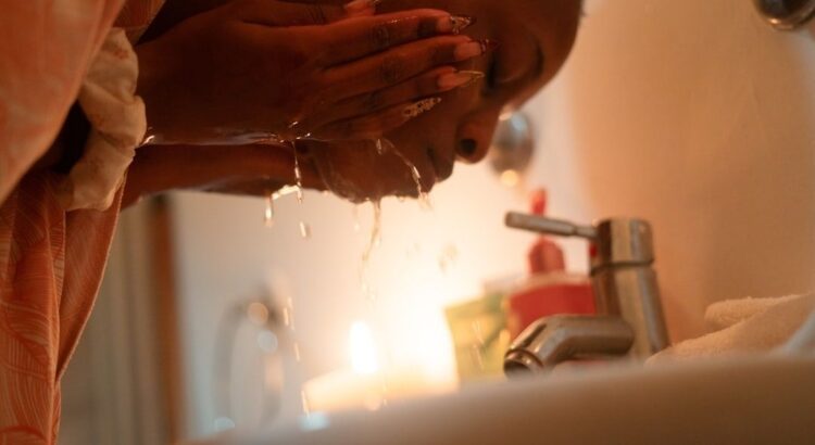 Person rinsing their face with water over a bathroom sink